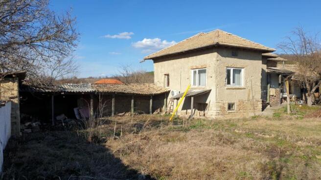 Exterior view of a traditional Bulgarian house with a tiled roof and adjacent outbuildings in a rural yard