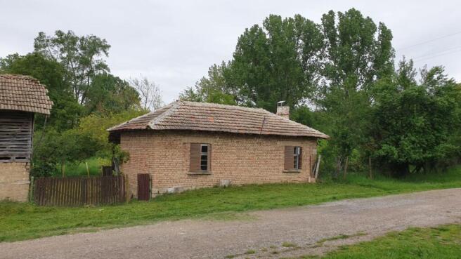 View of the small brick house with tiled roof and wooden shutters surrounded by greenery