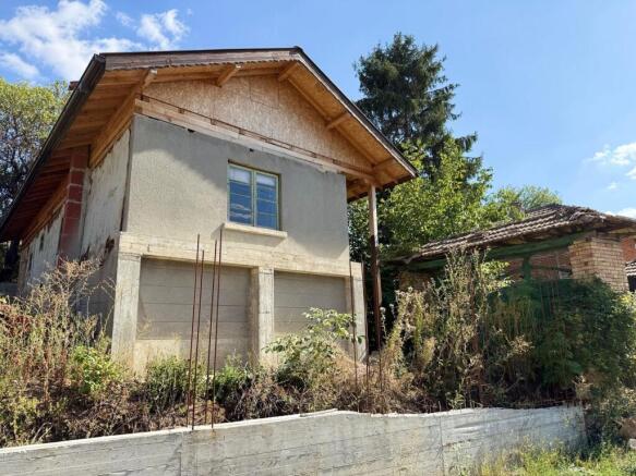 Exterior view of an old Bulgarian house showing new roof construction and chimney against a clear sky.