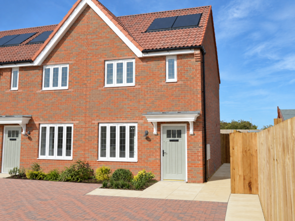 A modern red-brick house with white-framed windows and solar panels stands before a clear blue sky