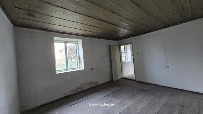 Interior view of an empty room featuring a wooden ceiling, white walls, wooden floor, and a window.