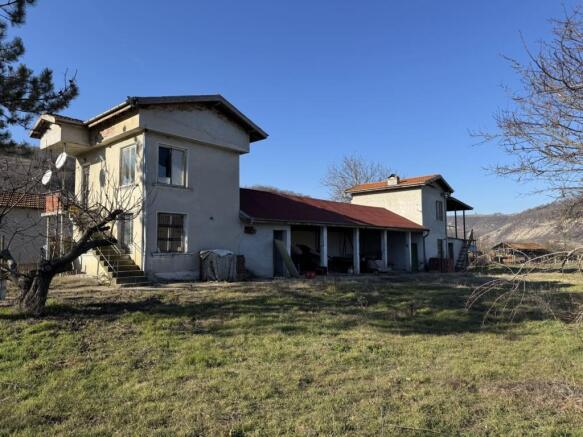 View of a two-story rural house with an attached single-story section and a grassy yard with leafless trees.