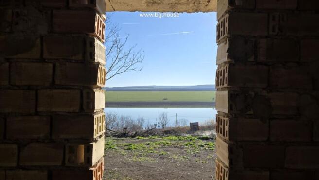View of lake and open fields seen through an unfinished brick wall opening in the villa.