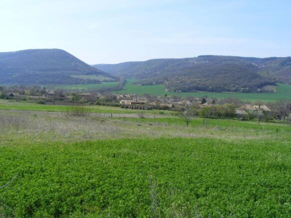 View of green fields and a village with forested hills in the distance under a clear sky