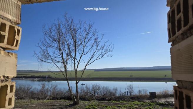 Lake and countryside view with a leafless tree visible through an opening in the unfinished brick walls.