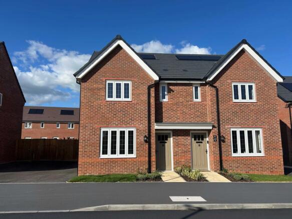 A pair of modern red-brick semi-detached houses with white-framed windows stand under a blue sky wit
