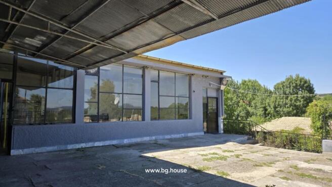 Covered terrace area with large windows and metal door, surrounded by trees and greenery