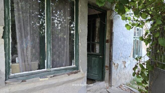 View of the house entrance showing a green wooden door and window with lace curtains on a textured plaster wall.
