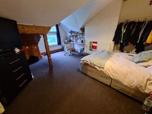 A cozy bedroom with a bed, some clothing hangin...