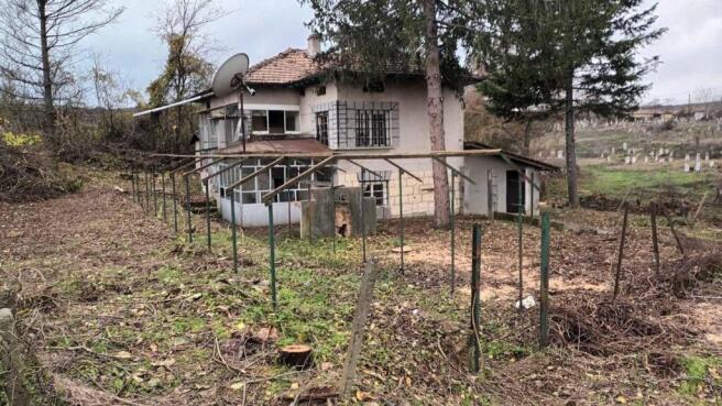 View of the two-storey house with a tiled roof, enclosed porch, and garden space with trees and fencing