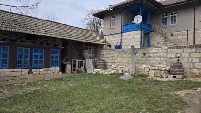 Stone retaining wall with adjacent wooden outbuilding painted dark brown with blue window frames