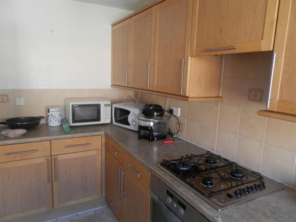 Compact fitted kitchen with light wood cabinets...
