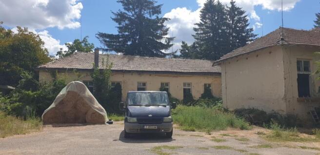 Open courtyard area featuring a blue van and stacked hay bales under plastic cover