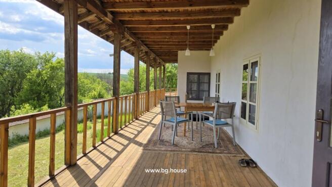Outdoor seating on the veranda with a wooden table and chairs, surrounded by trees and open landscape