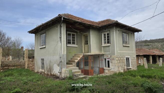 Two-storey house with greenish facade, tiled roof, and exterior stairs leading to the upper floor