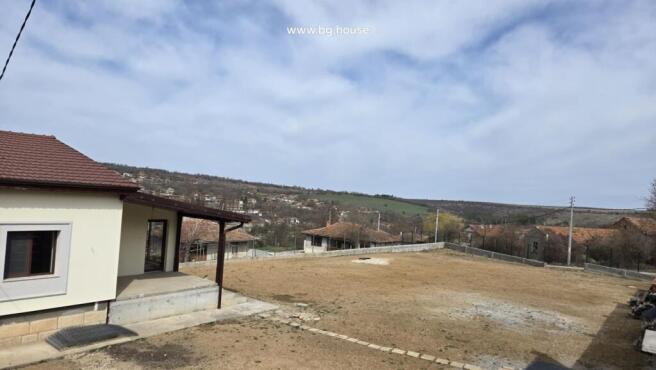 View of the house corner and large fenced yard with village houses and hills in the background