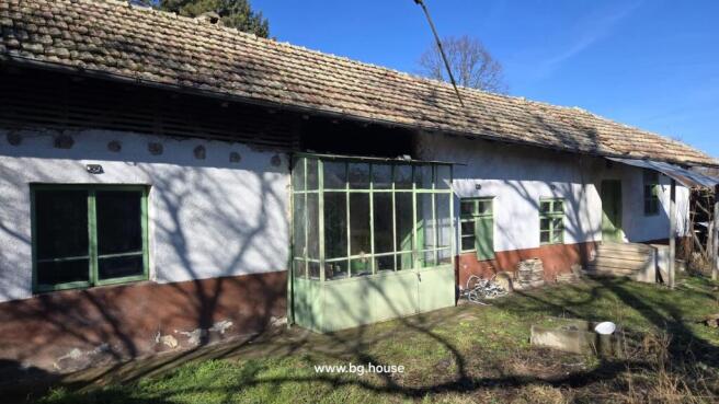 Front view of a traditional Bulgarian house with white and brown walls, green framed windows, and a tiled roof.