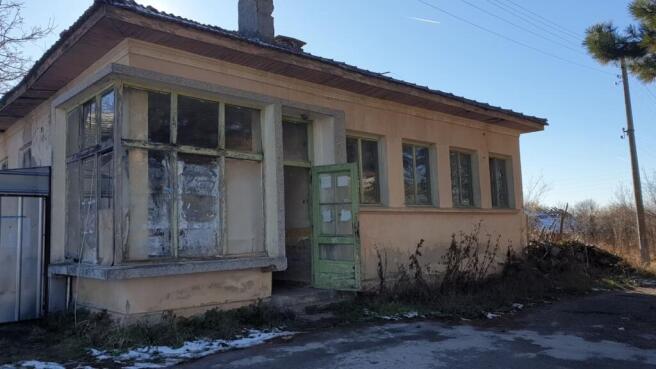 Exterior view of an old Bulgarian bakery building with multiple windows and a green wooden door open to the outside.