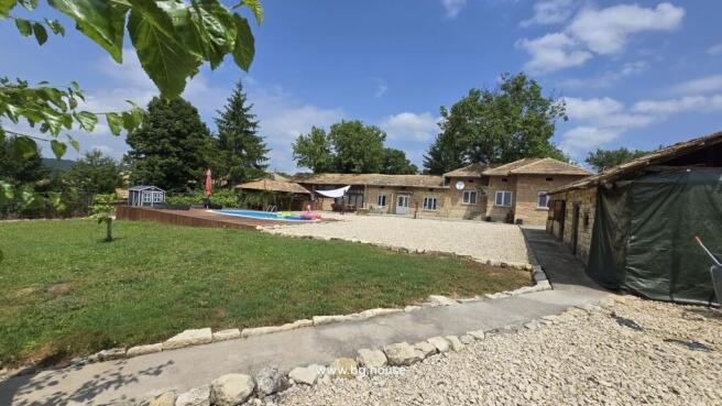 Outdoor view showing the Bulgarian house, swimming pool, garden, and surrounding trees under a partly cloudy sky.
