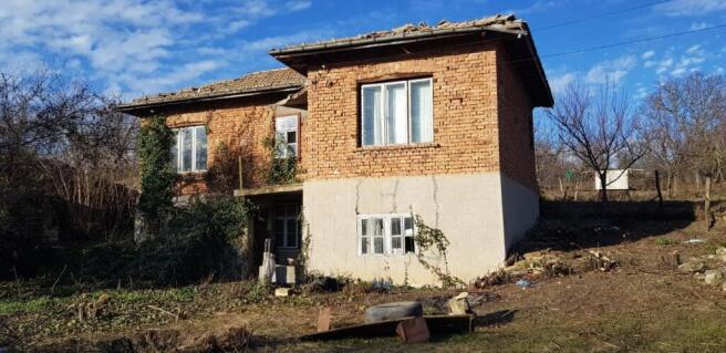 Side perspective of a two-storey rural house showing brick walls, white framed windows, and a tiled roof.