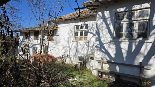 Side facade of the white cottage showing several windows and a wooden bench beside an overgrown garden area.