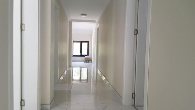 Bright indoor corridor with white walls, multiple doors, and window at end