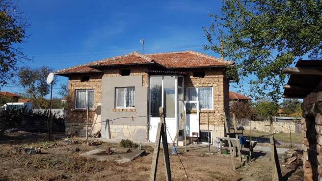 Side view of a small brick house with tiled roof and enclosed porch, dry garden and fencing