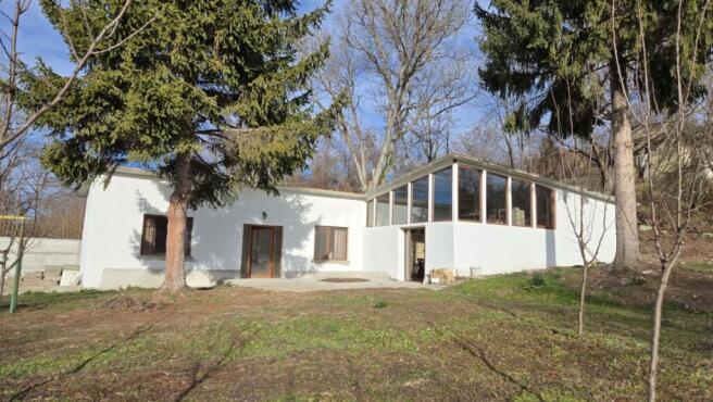 Exterior view of the renovated Bulgarian house showing white walls, large windows, and surrounding trees