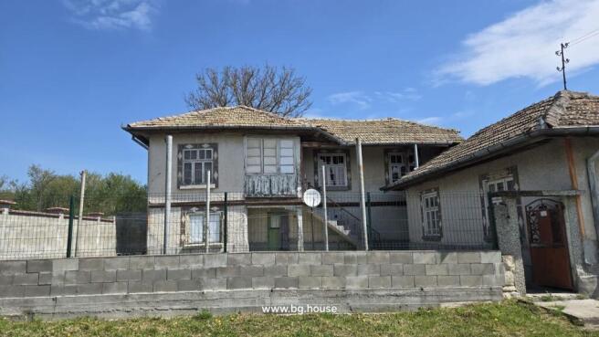 Front view of a traditional Bulgarian house showing tiled roof, multiple windows, and a fenced yard