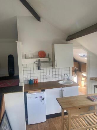 Compact kitchenette with white cabinetry, wood-...