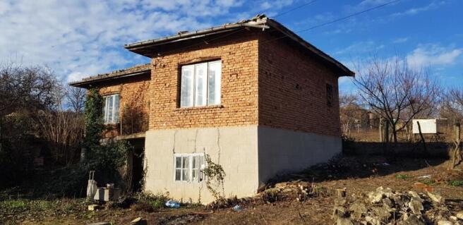 Alternate side angle showing the brick and stone construction of the rural house with a tiled roof and bare trees around.