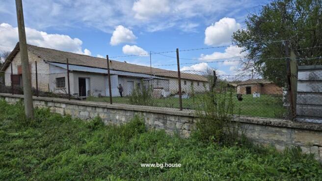 View of a farm building enclosed by a wire fence, showing a man standing near the entrance and green grass outside