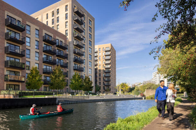 Two people walking down the canal with their arms around each other and two people in a canoe on the