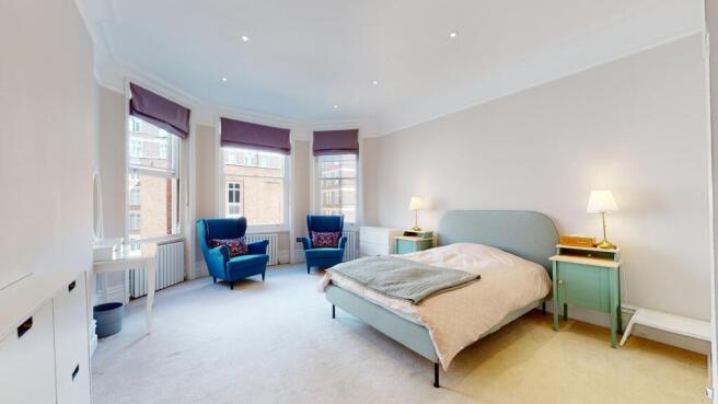 A spacious master bedroom with a stylish uphols...