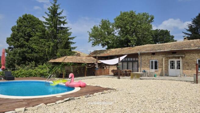 View of the house exterior featuring a round swimming pool with inflatables and a shaded seating area beside the house.