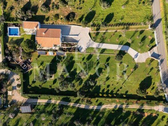Bird's-eye drone view of a brand new luxury villa for sale in Algarve, showcasing the private swimming pool, spacious garage, and sprawling 10,000 sqm landscaped plot near Estômbar.