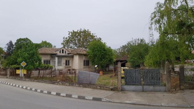 View of a single-storey house with a tiled roof surrounded by a wire fence and trees on a street corner