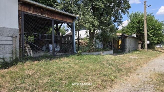 Covered outdoor storage area with wood piles and fenced garden alongside a rural dirt road