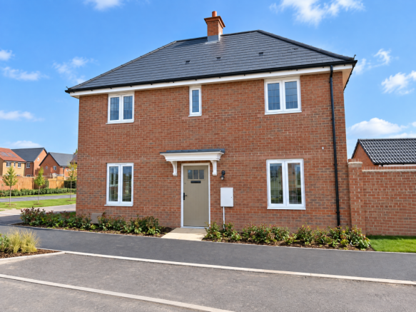 A modern two-story red brick house sits behind a paved driveway and small garden beds under a bright