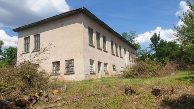 Side perspective of the old school building with barred windows and trimmed vegetation in the yard