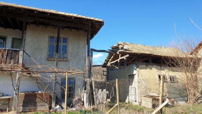 Side perspective showing traditional Bulgarian house with wooden balcony and adjacent outbuilding