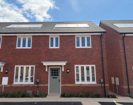 A modern red brick house with white-framed windows and a light green door stands in the foreground