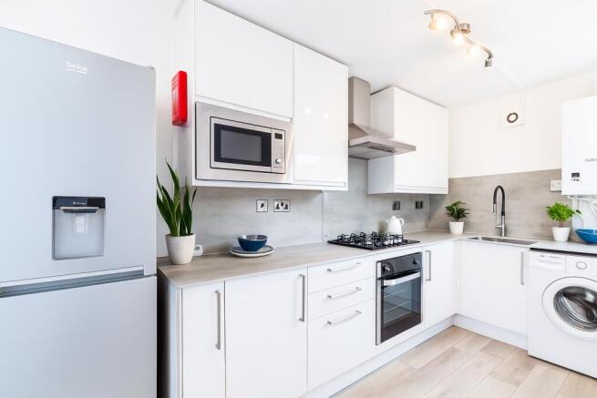 A modern, sleek kitchen featuring white cabinet...