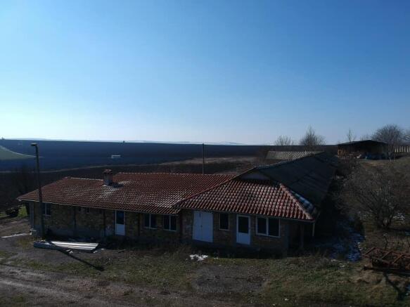 Stone farm building with red tiled roof viewed from above, with expansive fields in the background.