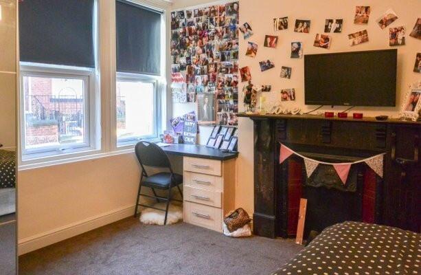A well-lit bedroom featuring a desk, a window w...