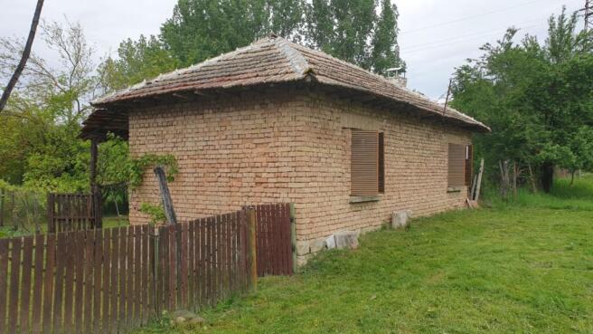 Side perspective showing brick walls, wooden shutters, and a wooden fence enclosing part of the garden