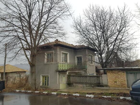 View of the two-storey Bulgarian house showing the balcony and surrounding bare trees in winter
