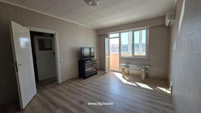 Bright living room featuring light wood flooring, patterned wallpaper, a TV on a black chest of drawers, and an open door leading to the balcony.