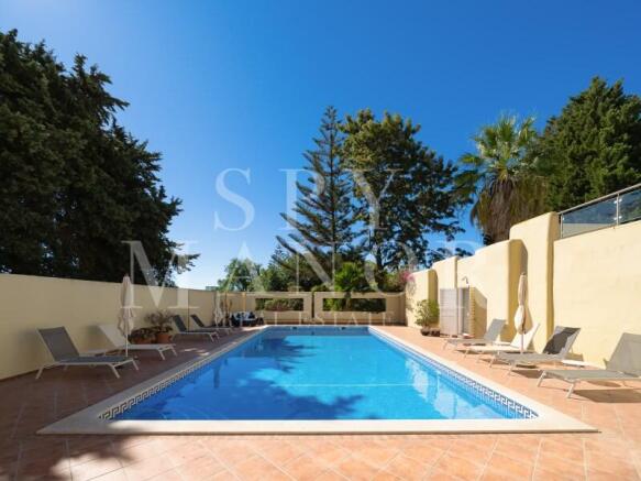 Large swimming pool with sunbeds and paved terrace at a luxury villa for sale in Carvoeiro Clube, Algarve, surrounded by mature trees.