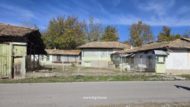 Front view of a traditional Bulgarian house with multiple tiled roofs and a fenced yard in Kovachevets village